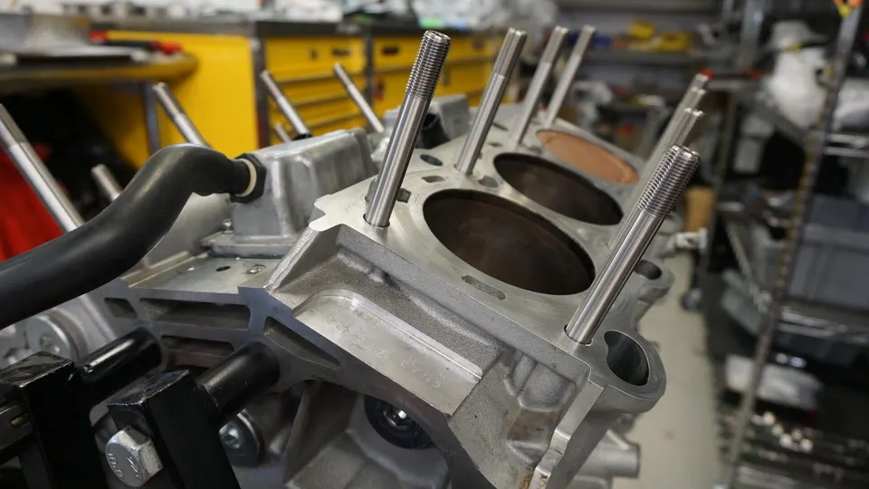 Close-up of an engine block with cylinder bores and head studs during assembly in a performance tuning shop.