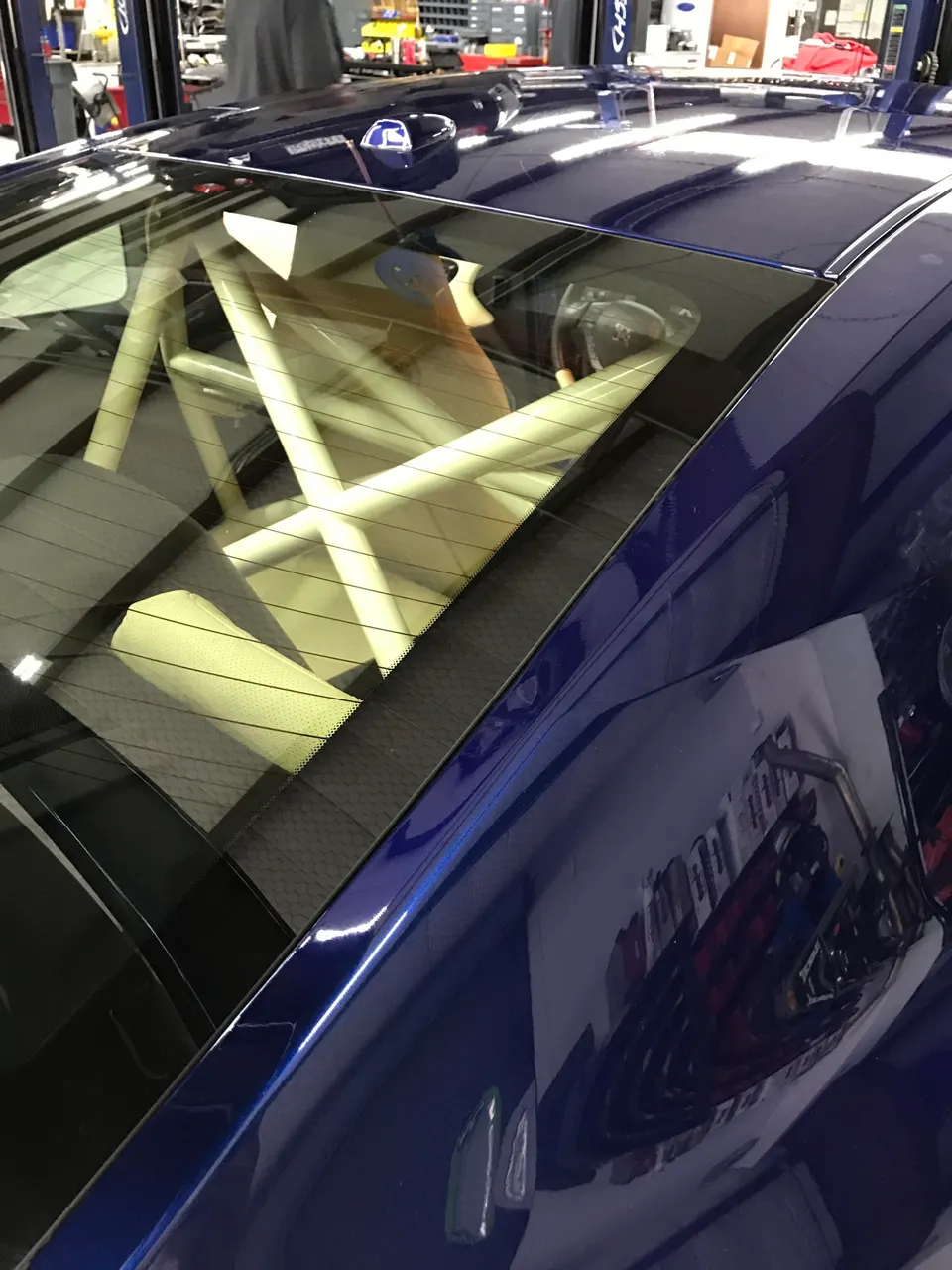 Blue sports car with a roll cage visible through the rear window, parked in a performance tuning shop.