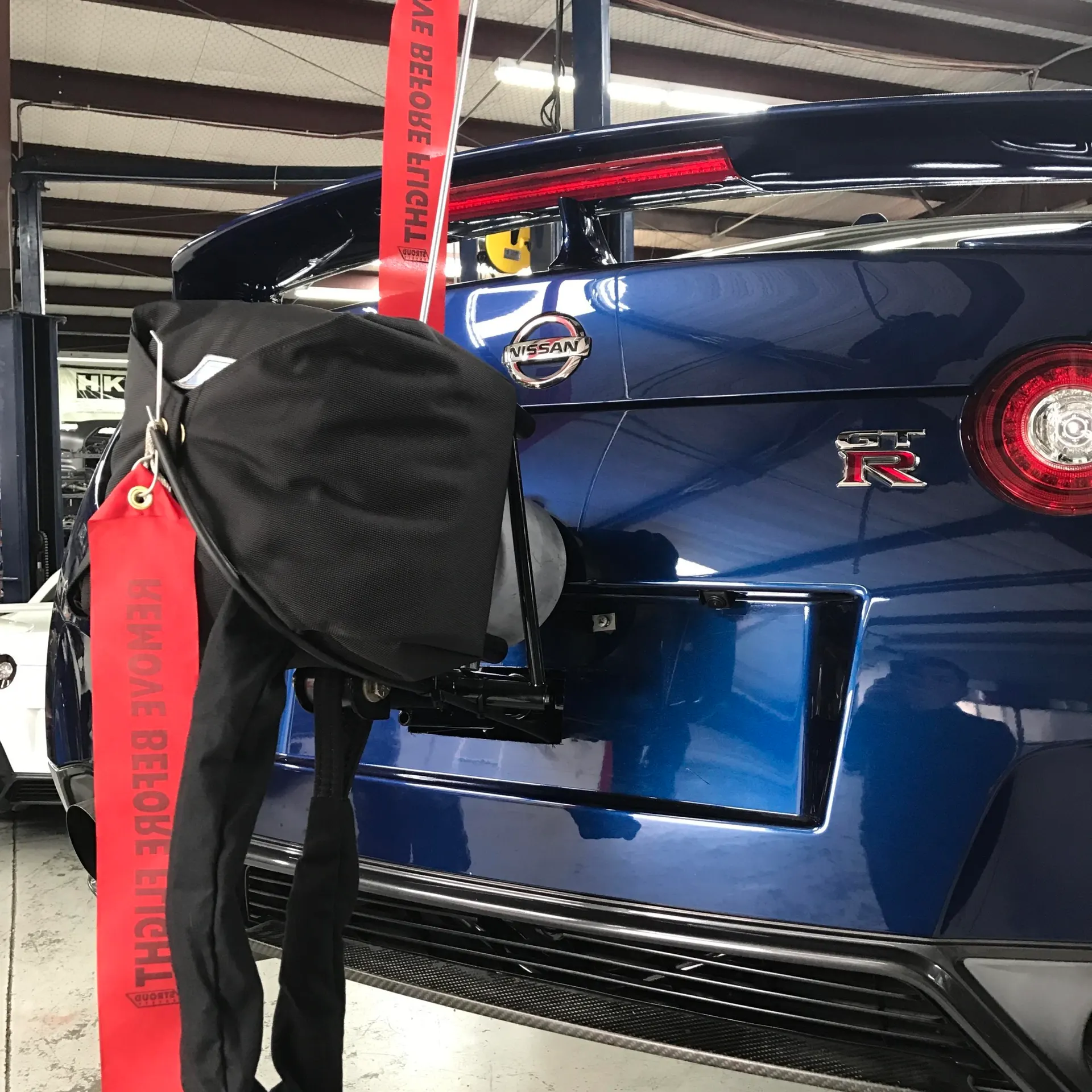 A blue Nissan GT-R in a performance shop with a covered exhaust system and a red "REMOVE BEFORE FLIGHT" tag.