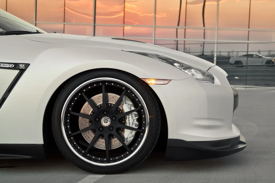 Close-up of a white Nissan GT-R's front wheel, featuring black aftermarket forged wheels and Brembo performance brakes.