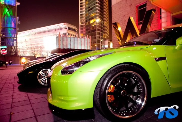 Lime green Nissan GT-R and a black Lamborghini parked at night in a vibrant city setting with custom wheels.