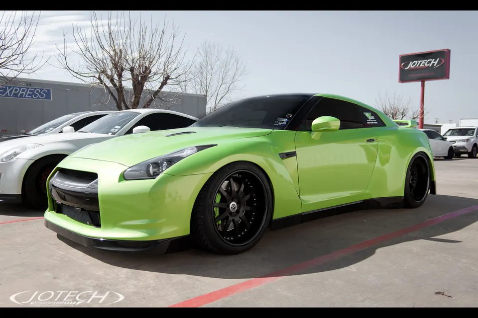 A vibrant lime green Nissan GT-R with black aftermarket wheels parked outside the Jotech Motorsports facility.