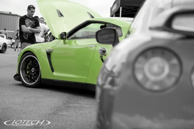 A vibrant green Nissan GT-R with its hood open, parked at a car show, with a person observing the engine bay.