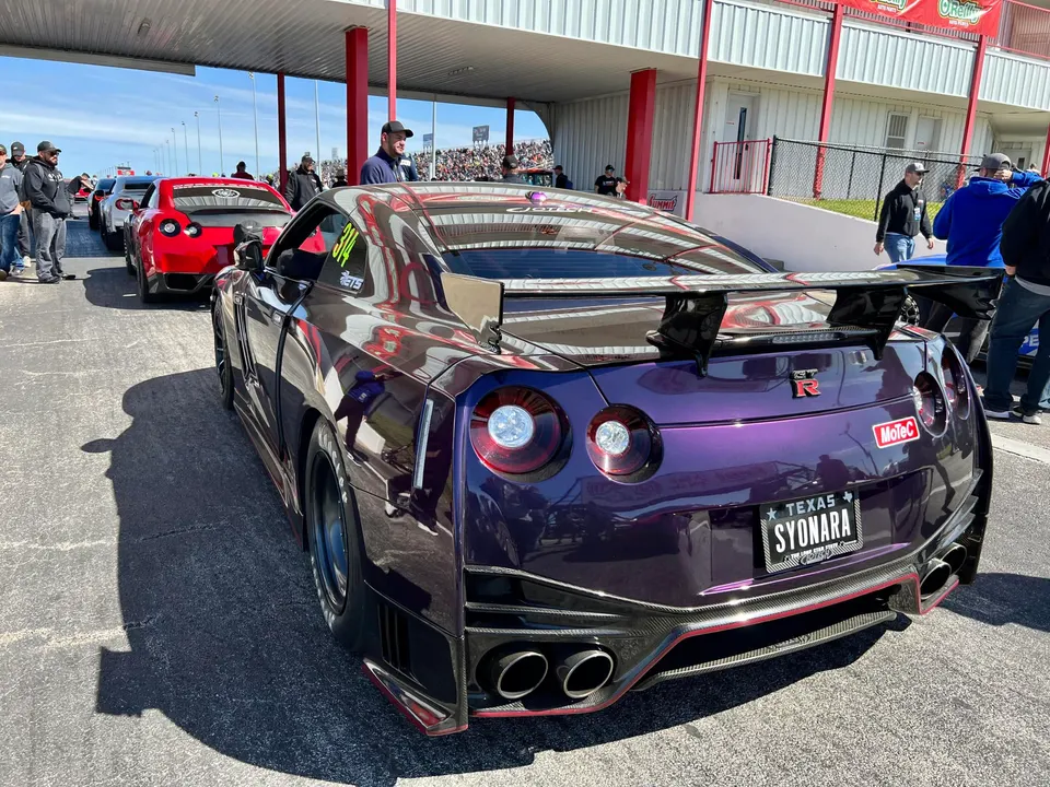 A custom purple Nissan GT-R with a large rear wing and carbon fiber diffuser in a drag strip staging lane.