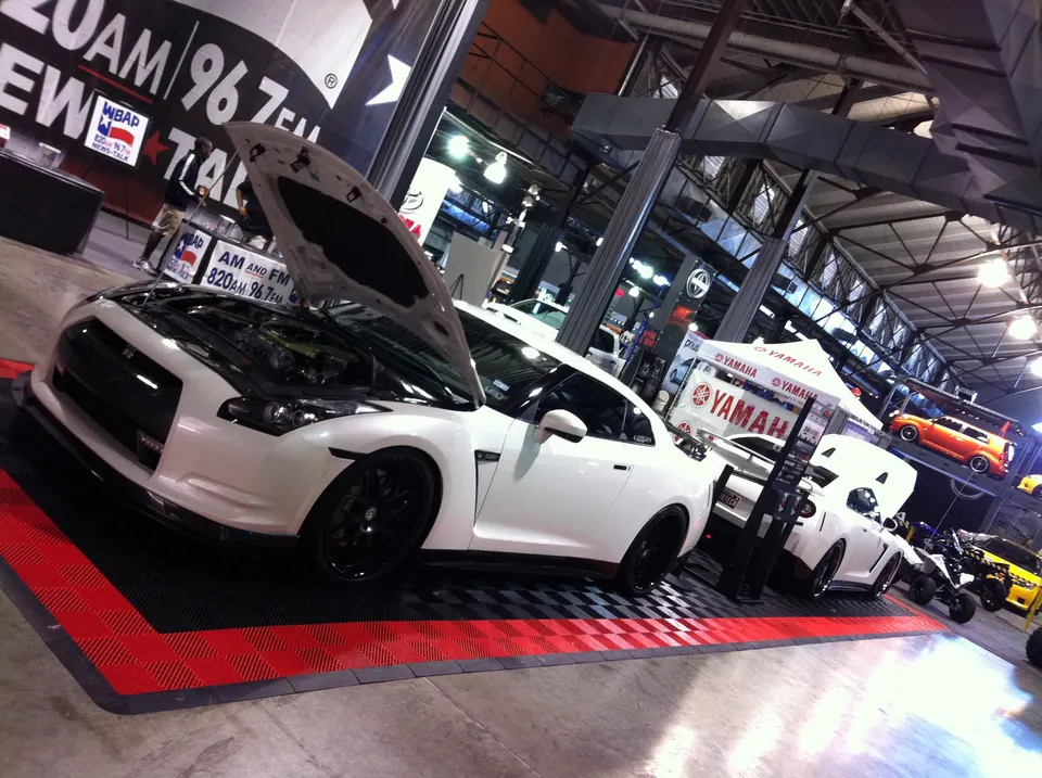 White Nissan GT-R with its hood open on display at an indoor car show, showcasing its engine bay and custom wheels.