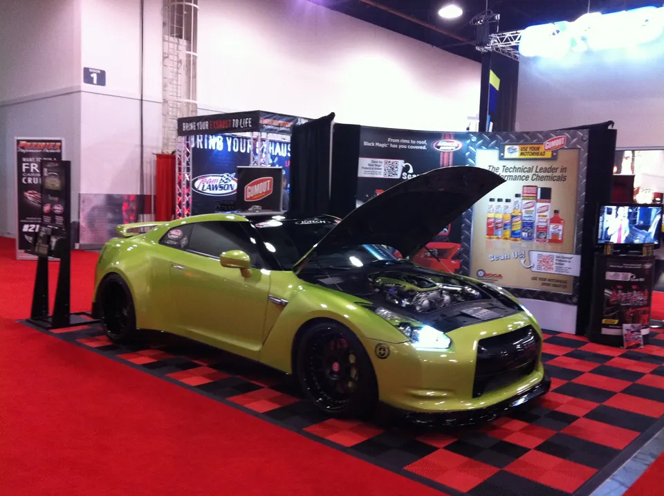 A lime green Nissan GT-R with its hood open on display at a car show, showcasing its engine bay and custom wheels.