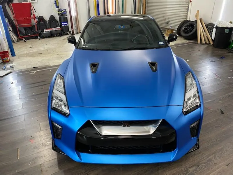 Front view of a matte blue Nissan GT-R R35 parked in a performance tuning shop.