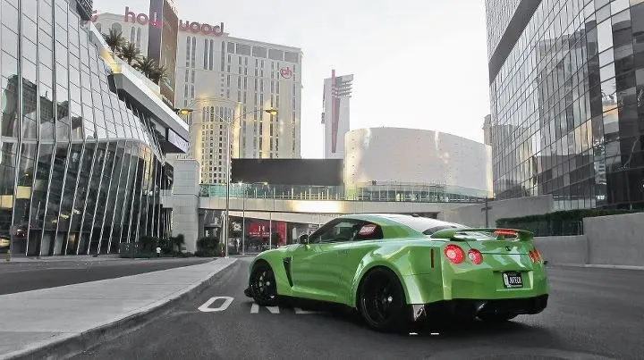 A vibrant green Nissan GT-R R35 with aftermarket wheels parked on a city street in Las Vegas, surrounded by modern buildings.