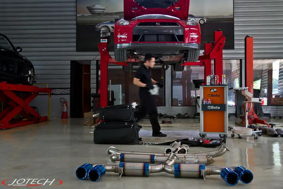 A red Nissan GT-R on a lift in a Jotech Motorsports shop with a new exhaust system on the floor.