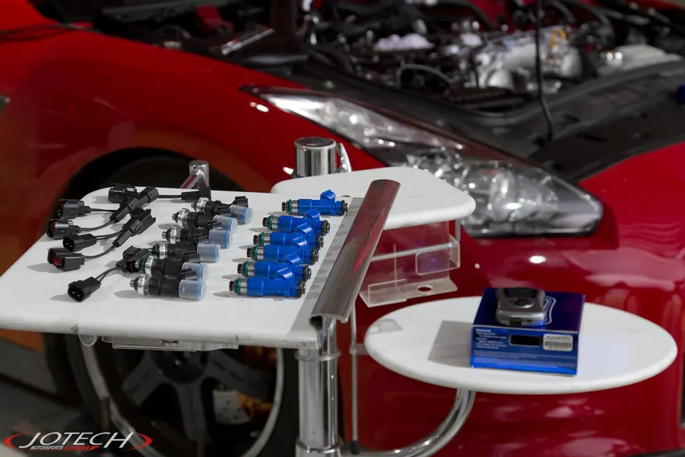 Fuel injectors and wiring harnesses on a table in front of a red Nissan GT-R with its hood open at Jotech Motorsports.