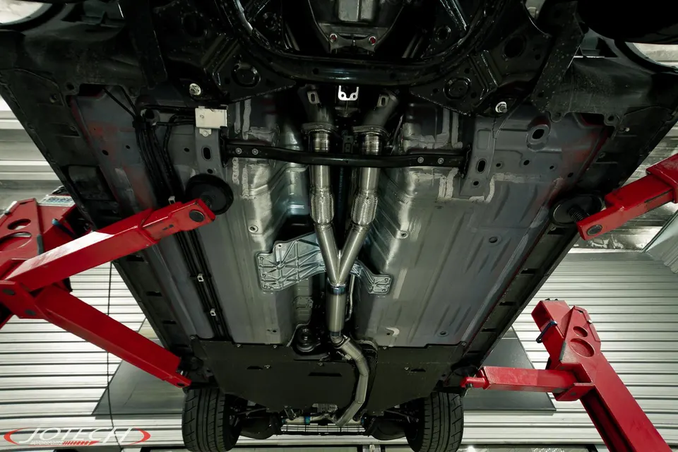 Underside view of a performance car on a lift, showcasing a newly installed stainless steel exhaust system in a tuning shop.