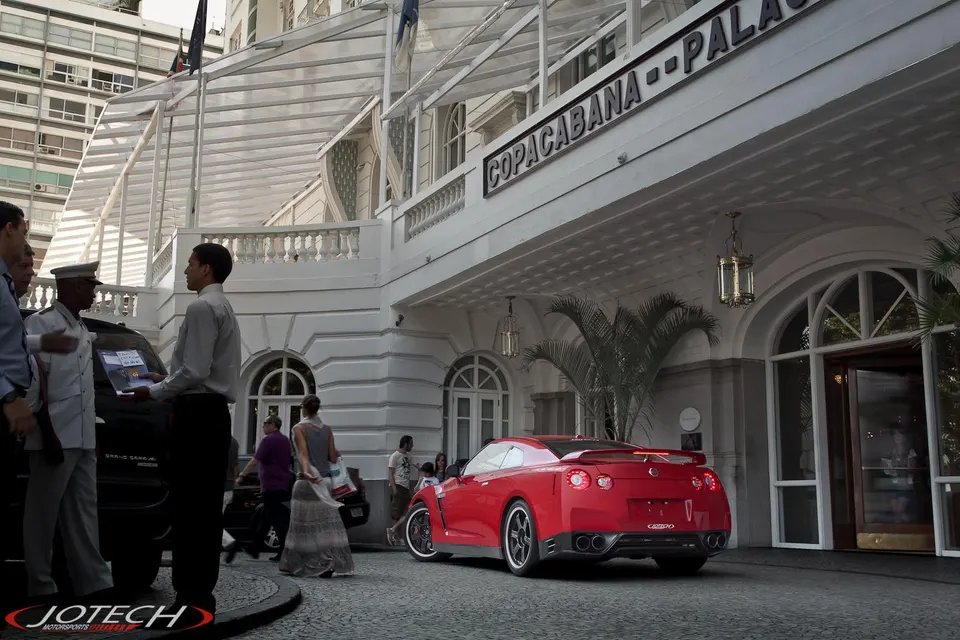 Red Nissan GT-R parked in front of the historic Copacabana Palace hotel in Rio de Janeiro with people around.