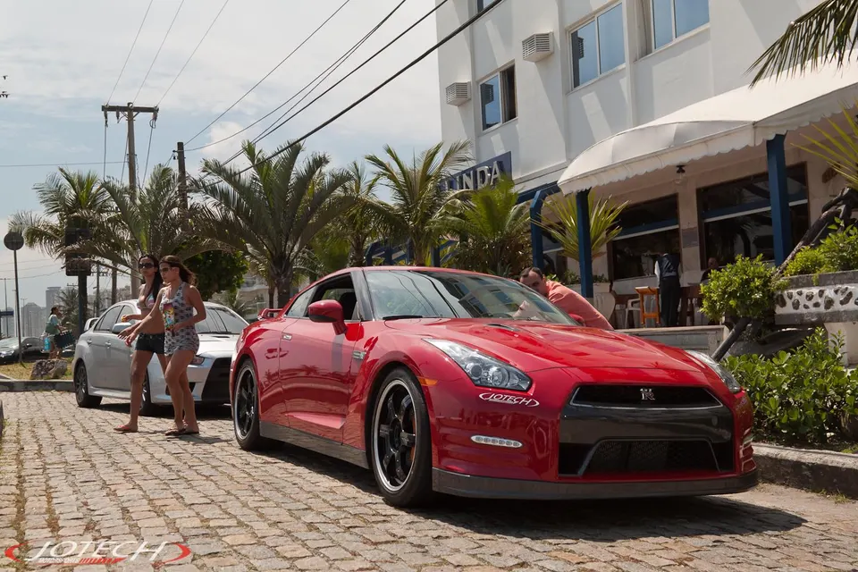 Red Nissan GT-R parked on a cobblestone street with people and palm trees in the background.