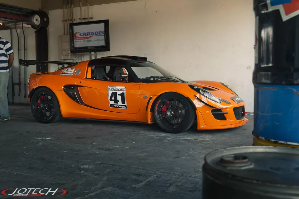 Orange Lotus race car with number 41 parked in a pit garage, featuring a large rear wing and black wheels.