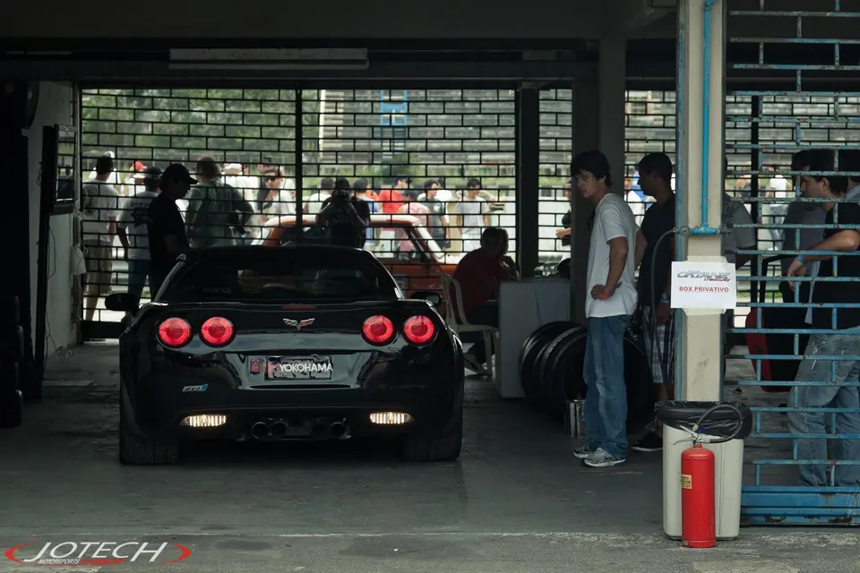 Black Corvette C6 ZR1 parked in a pit area with people standing around, Yokohama license plate frame visible.