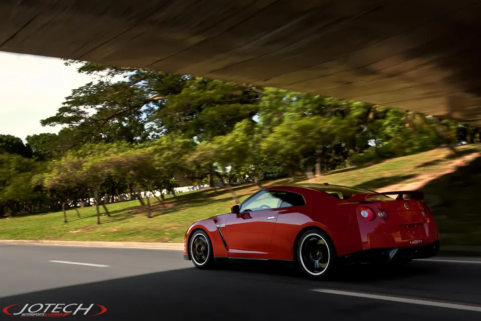 Red Nissan GT-R driving on a road under an overpass, showcasing its sleek design and performance.