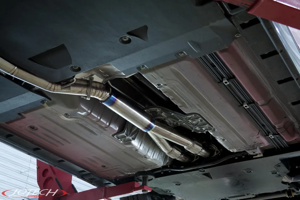 Underside view of a car on a lift showcasing a Jotech titanium exhaust system with blue burnt tips.