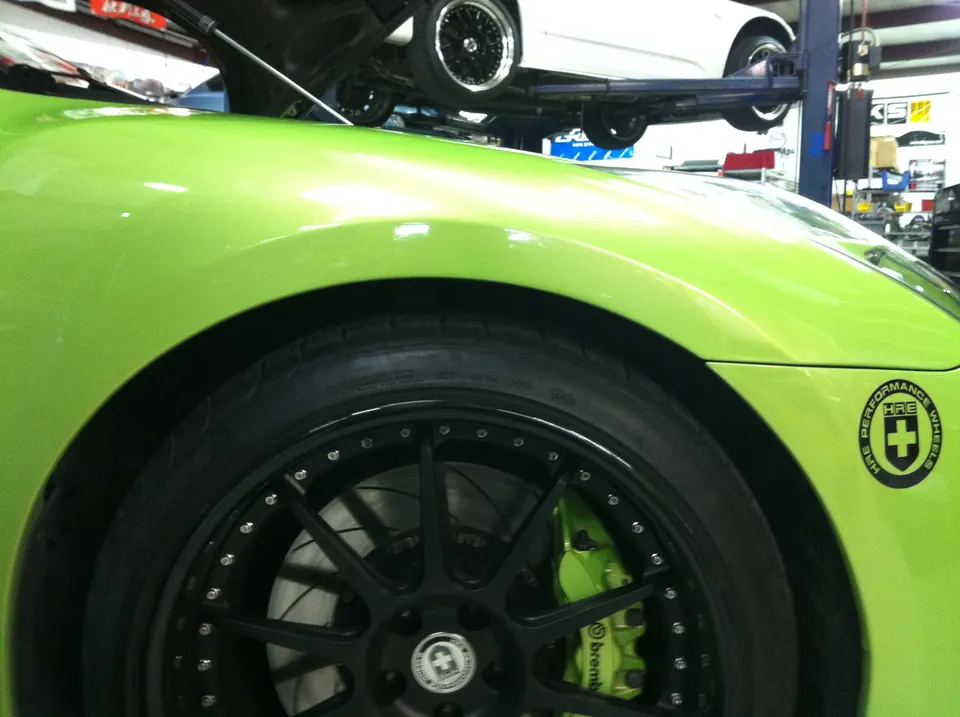 Close-up of a bright green car's front wheel with black HRE wheels and green Brembo brakes in a shop.