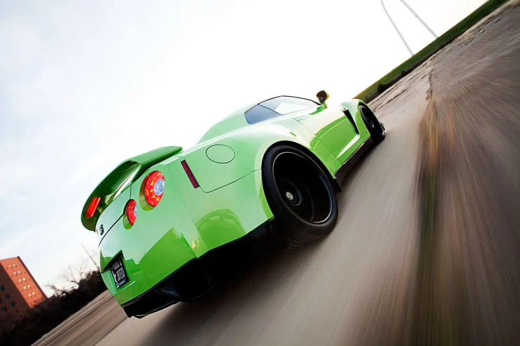 Green Nissan GT-R with custom paint and black wheels speeding on a road with motion blur, captured from a low angle.