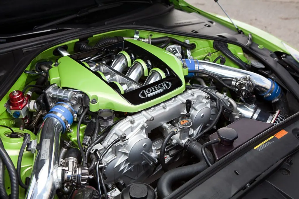 Close-up of a highly modified Jotech Nissan GT-R engine bay featuring a custom green intake manifold and chrome boost piping.