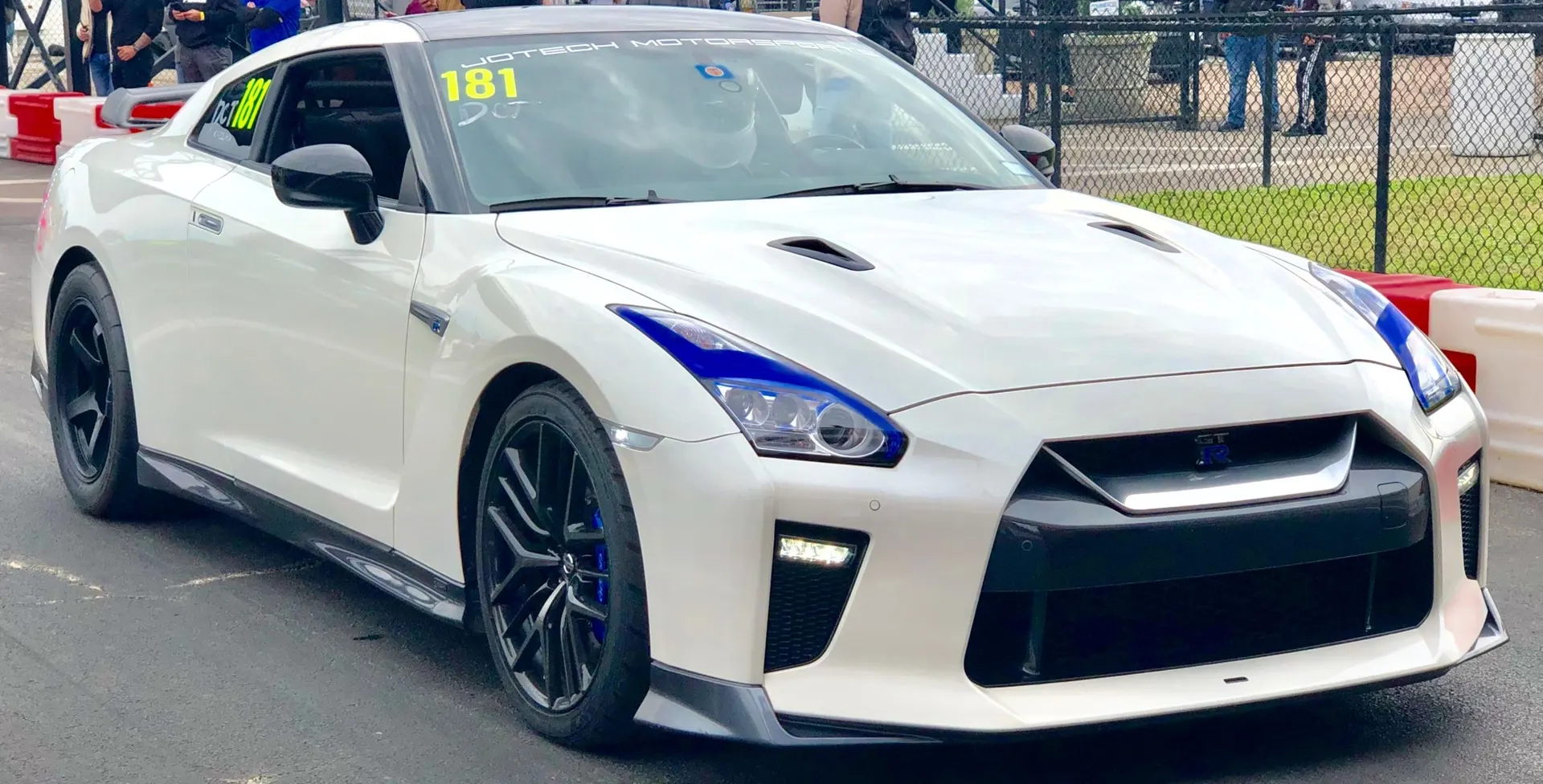 A white Nissan GT-R with blue accents and race numbers on the side and windshield at a drag strip.