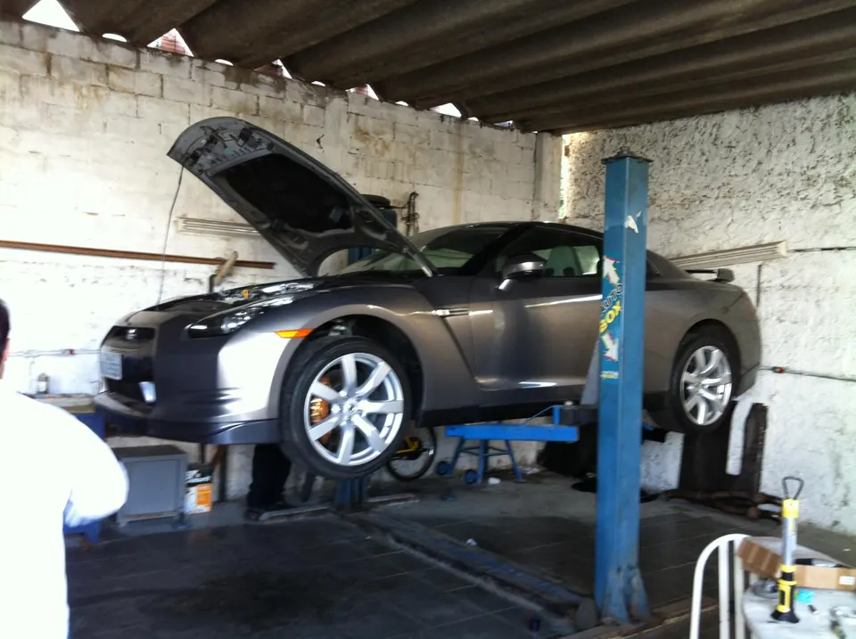 Grey Nissan GT-R on a car lift with its hood open in a shop, undergoing maintenance or modifications.