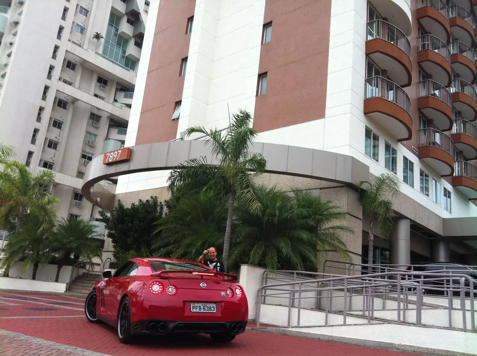 Red Nissan GT-R parked in front of a modern building with a man standing next to it, surrounded by palm trees.