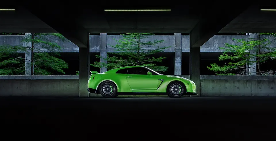 A vibrant green Nissan GT-R R35 with custom wheels parked in a concrete structure with trees in the background.