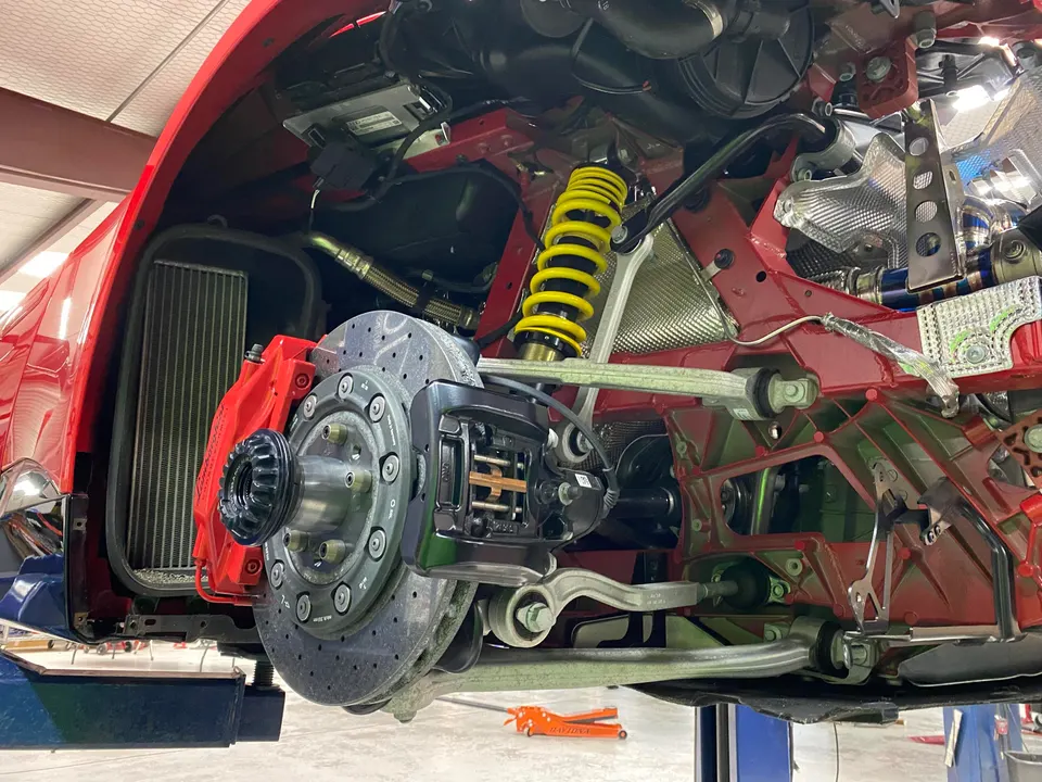 Red car on a lift in a shop, showcasing the suspension, yellow coilover, red brake caliper, and drilled rotor.
