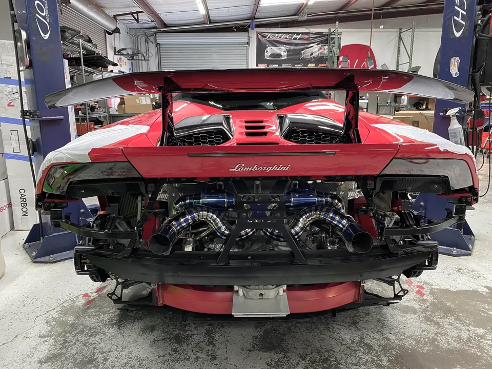 Rear view of a red Lamborghini Huracan in a performance shop with its bumper removed, showcasing a custom turbo and exhaust system.