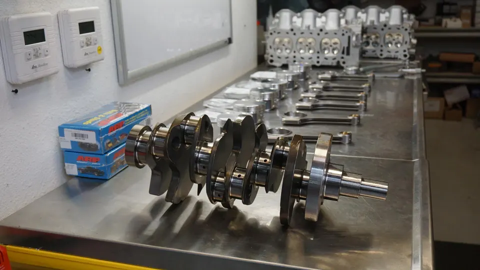 Crankshaft, pistons, connecting rods, and cylinder heads laid out on a workbench for an engine build.