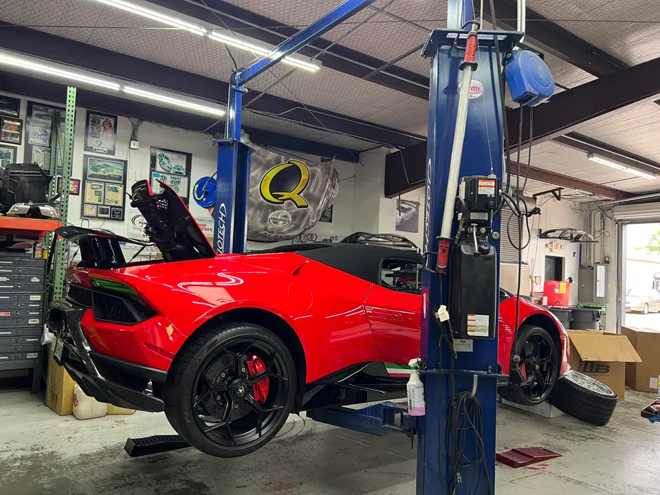 A red Lamborghini Huracan convertible on a car lift in a performance tuning shop with its engine bay open.