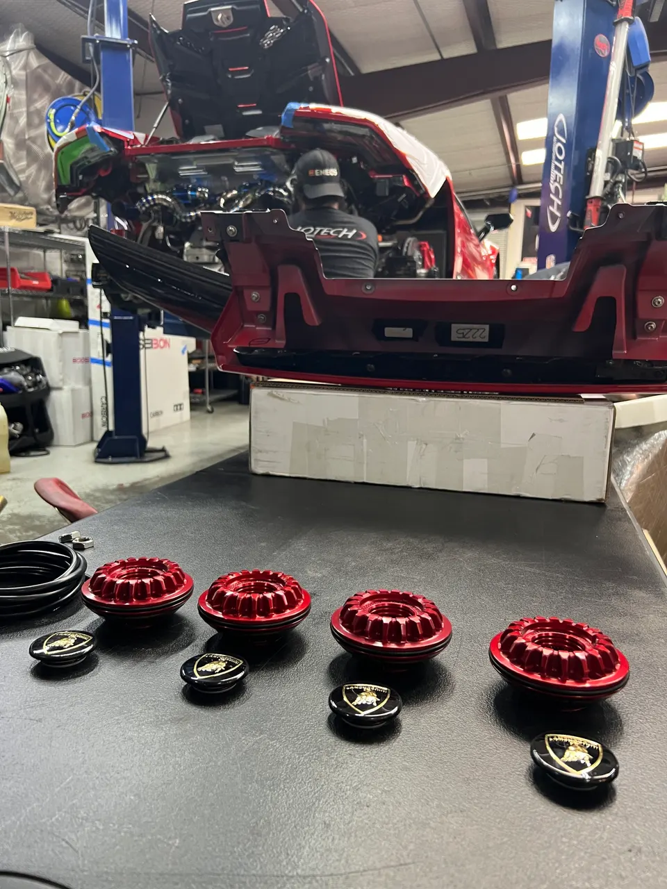 Lamborghini Huracan undergoing maintenance in a performance shop with red machined parts and wheel center caps on a workbench.