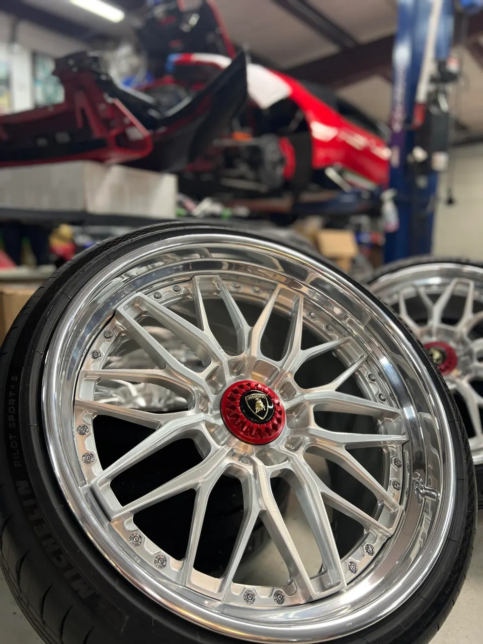 Close-up of a custom silver Lamborghini wheel with Michelin tires in a performance shop.