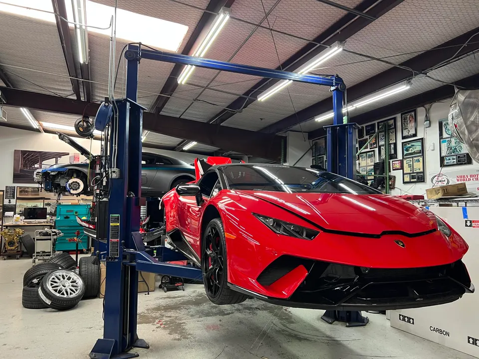 Red Lamborghini Huracan on a car lift in a performance tuning shop with another car on a lift in the background.