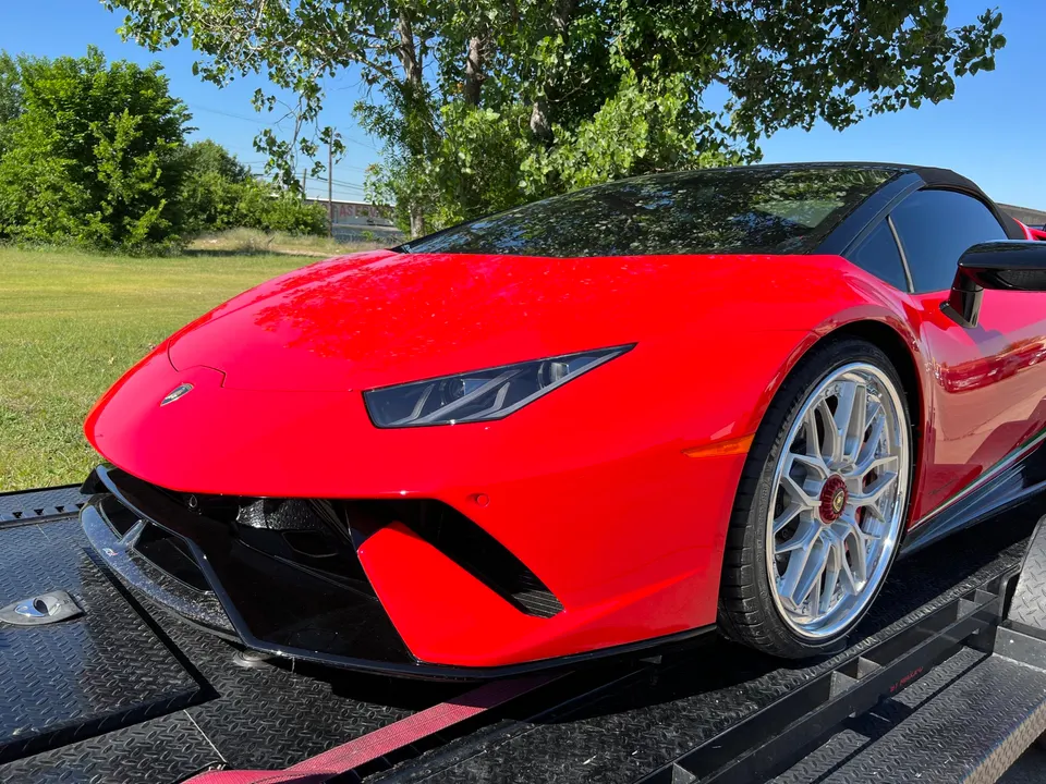 Red Lamborghini Huracan supercar with custom silver wheels on a car hauler trailer under a clear sky.