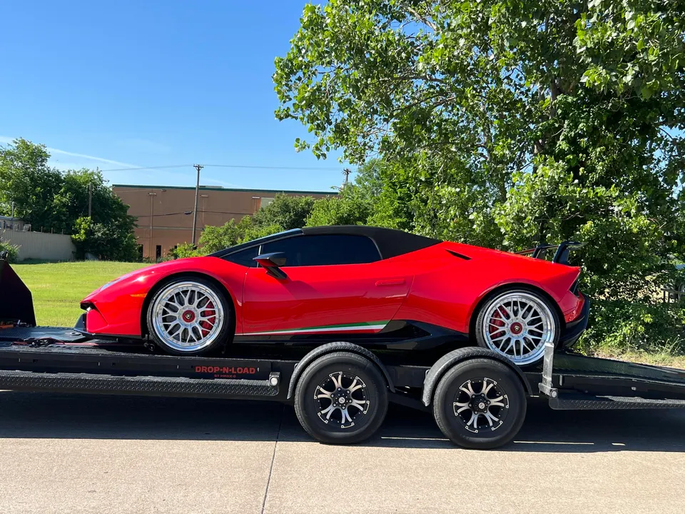 Red Lamborghini Huracan convertible with aftermarket wheels and a rear wing being transported on a car hauler.