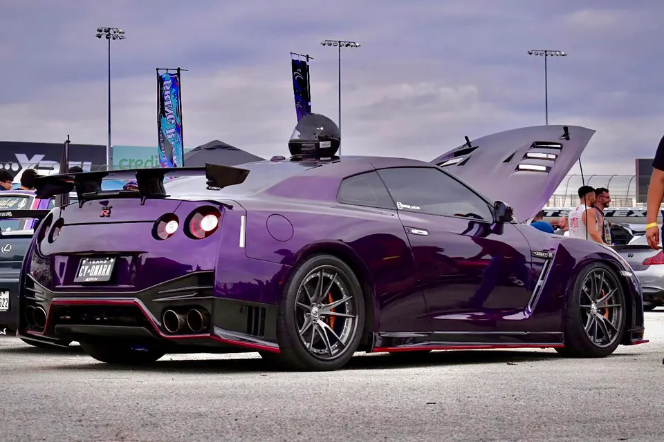 Purple widebody Nissan GT-R with aftermarket wheels and a large rear wing at an outdoor car event.