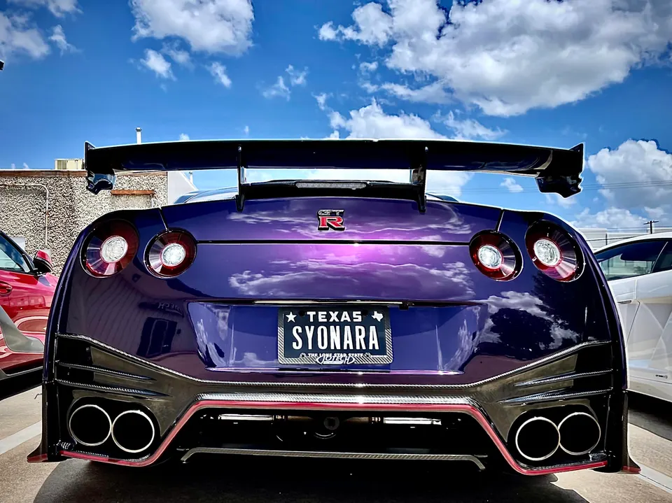 Rear view of a custom purple Nissan GT-R with a large aftermarket wing, custom diffuser, and quad exhaust tips.
