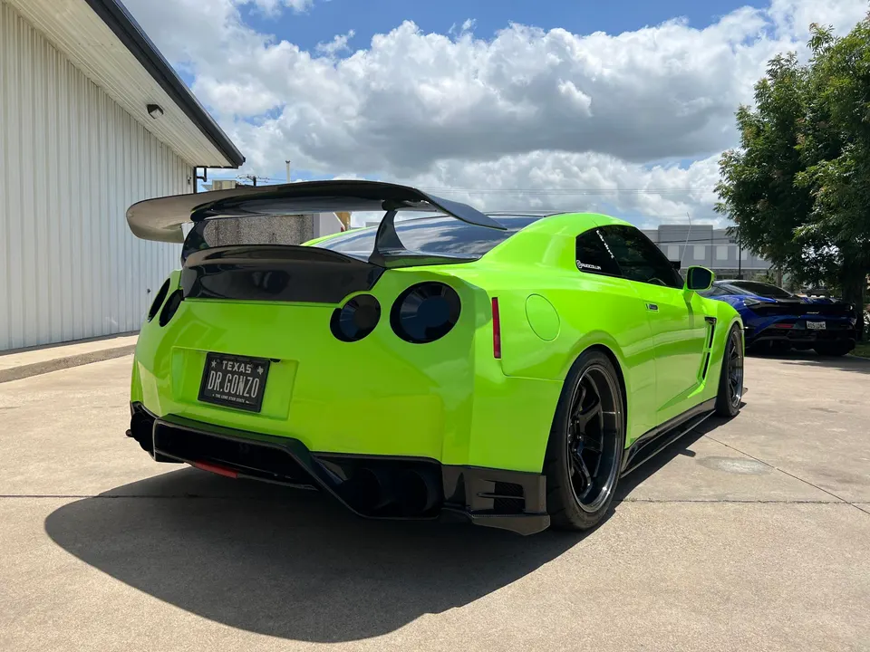 Lime green Nissan GT-R with a large carbon fiber rear wing and diffuser parked outdoors on a sunny day