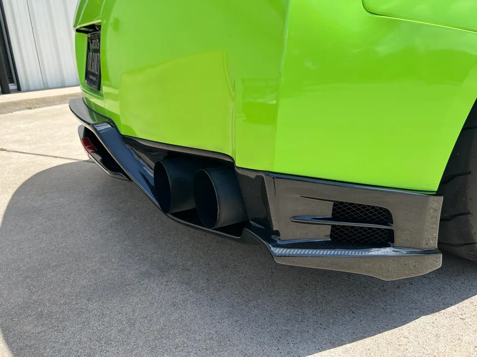 A bright green Nissan GT-R showcasing its carbon fiber rear diffuser and large aftermarket exhaust tips.