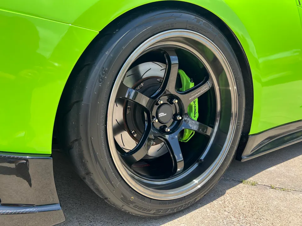 A close-up of a bright green car's black Advan Racing wheel, green Brembo brake caliper, and Toyo tire.
