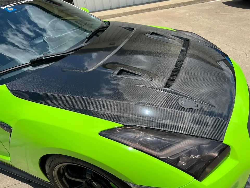 Close-up of a lime green Nissan GT-R with a custom carbon fiber hood featuring vents and hood pins.
