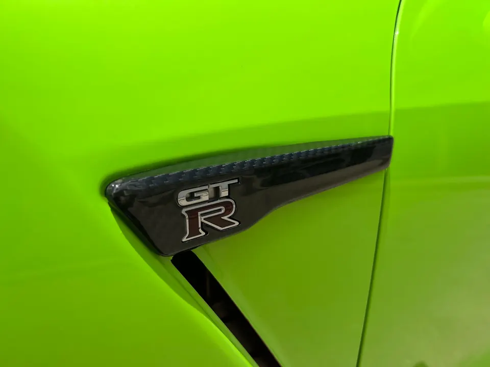 Close-up of a bright green Nissan GT-R fender with a carbon fiber vent and GT-R emblem.
