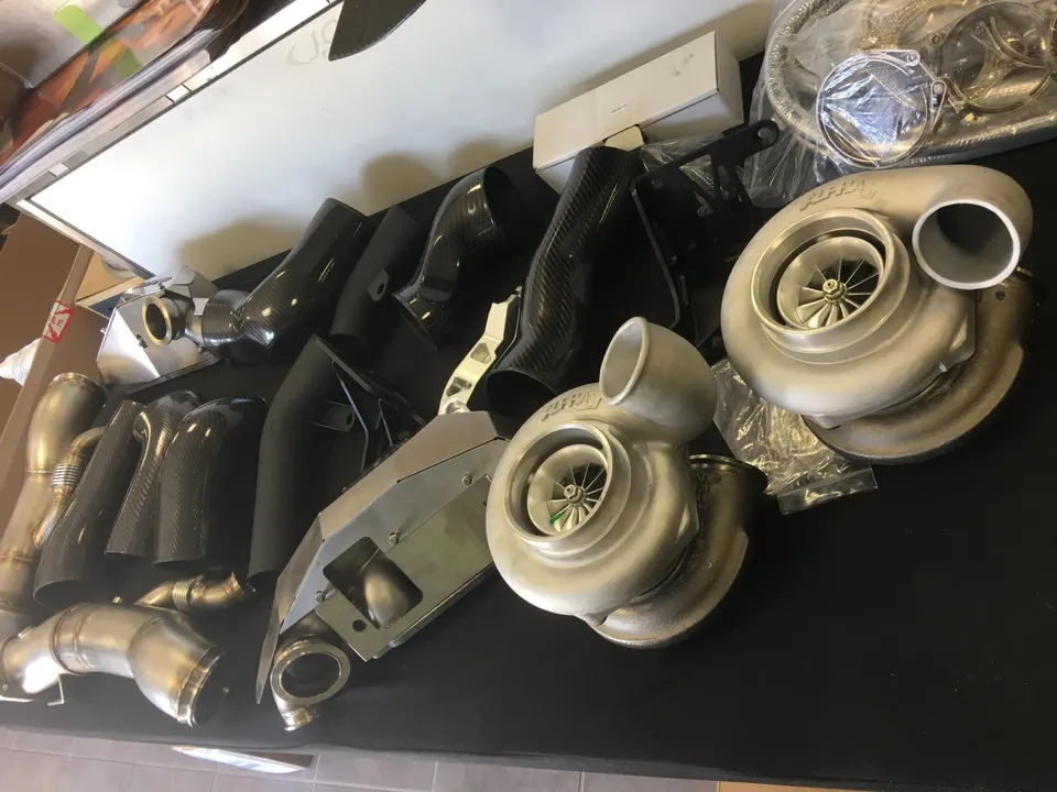 High-performance turbochargers, carbon fiber intake pipes, and stainless steel exhaust components laid out in a shop.