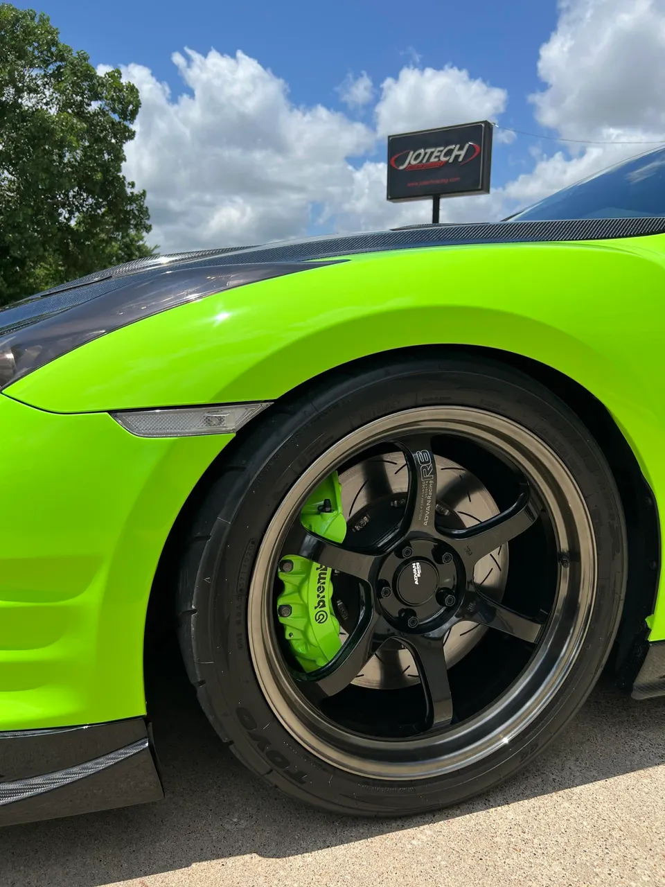 Close-up of a bright green Nissan GT-R with Advan Racing R6 wheels and green Brembo brakes at Jotech Motorsports.