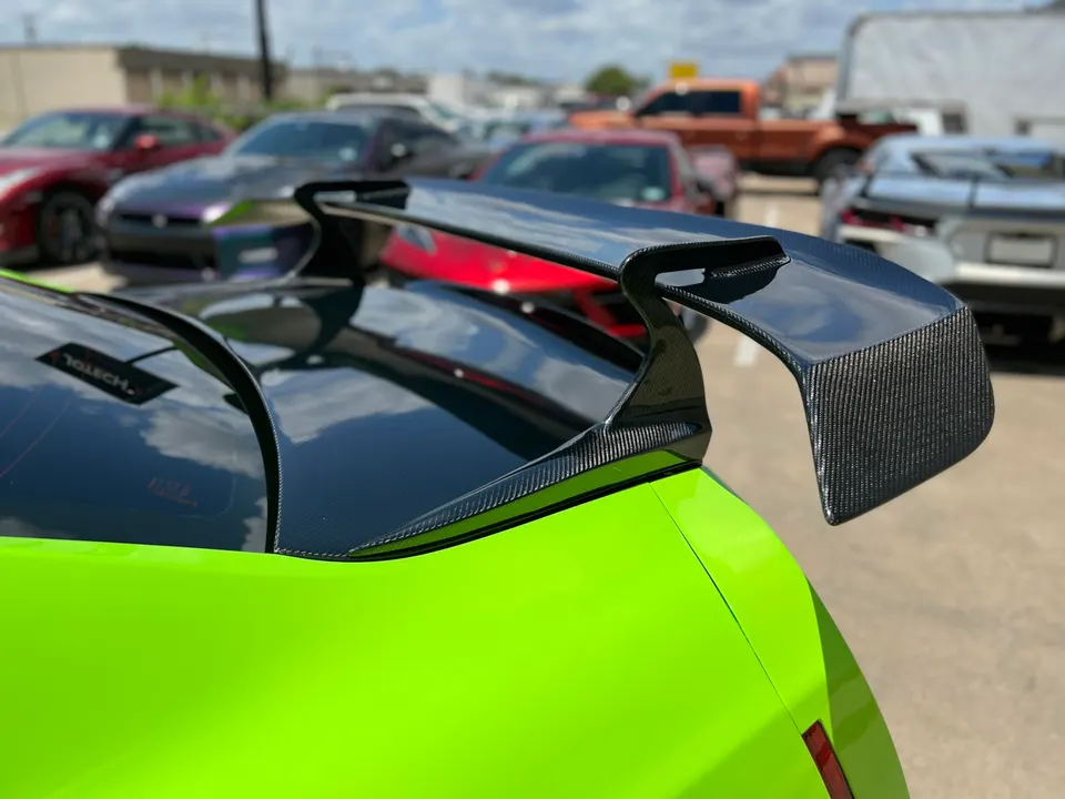 Close-up of a bright green sports car's carbon fiber rear wing in a parking lot.