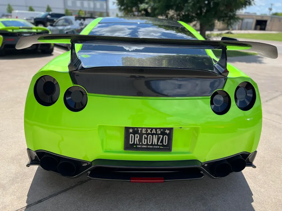 Rear view of a lime green Nissan GT-R with a large carbon fiber wing and aftermarket exhaust tips.