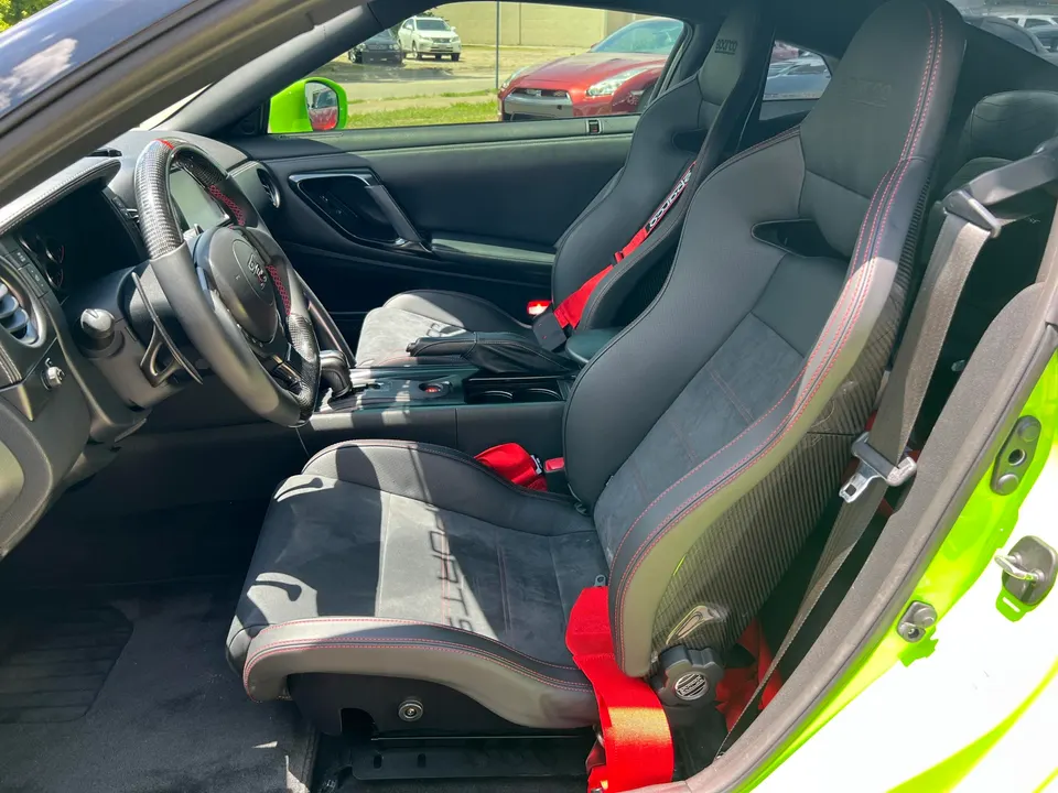 Interior view of a Nissan GT-R featuring Sparco racing seats with red harnesses and a custom carbon fiber steering wheel.