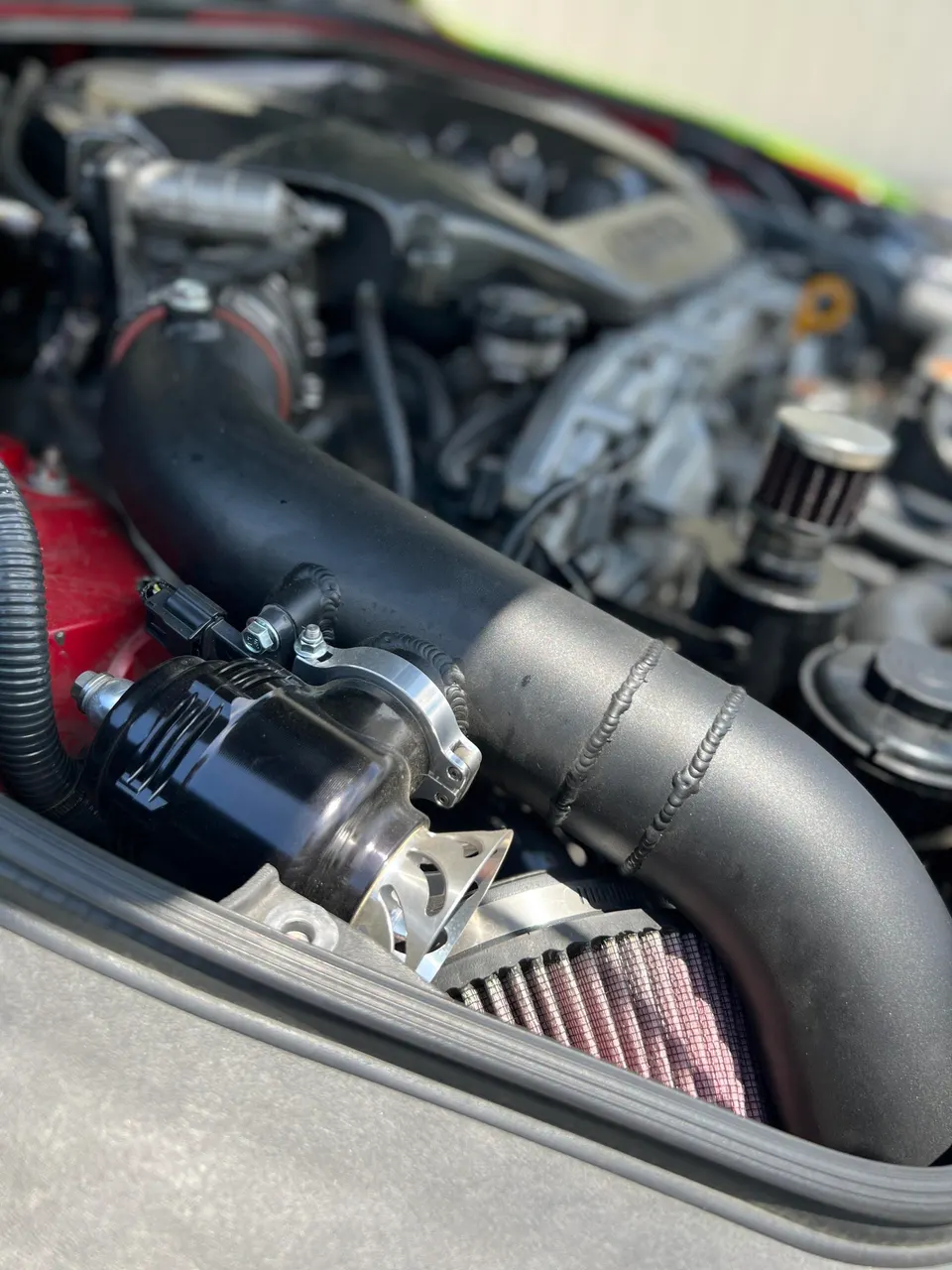 Close-up of a car's engine bay showing an aftermarket intake system, air filter, and blow-off valve.